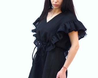May include: A black linen dress with a ruffled neckline and sleeves. The dress has a drawstring waist and a short, A-line silhouette.
