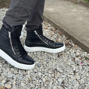 May include: A pair of black leather high-top trainers with white soles and a zip detail on the side.