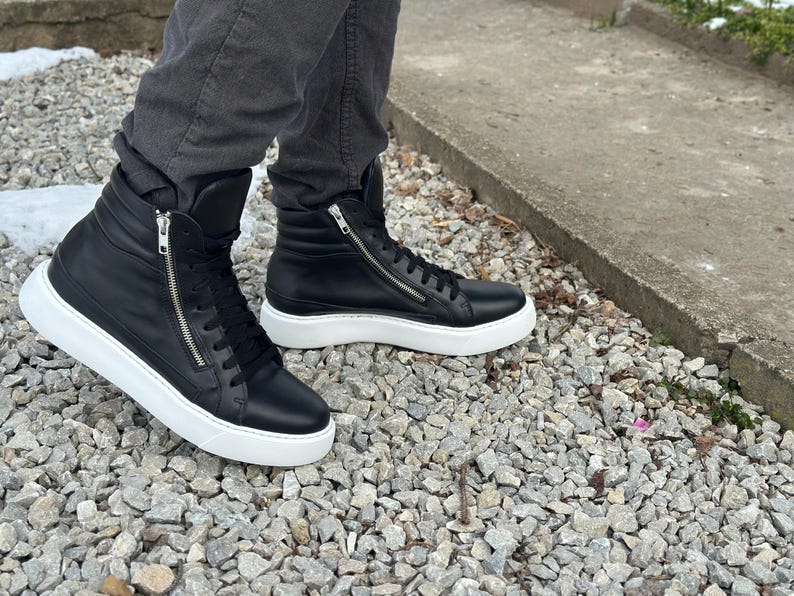 May include: A pair of black leather high-top trainers with white soles and a zip detail on the side.