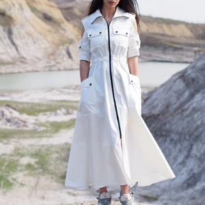 May include: A white long-sleeved dress with a zipper closure, a cinched waist, and cut-out shoulders. The dress has two large pockets on the front and is worn with gray sneakers.