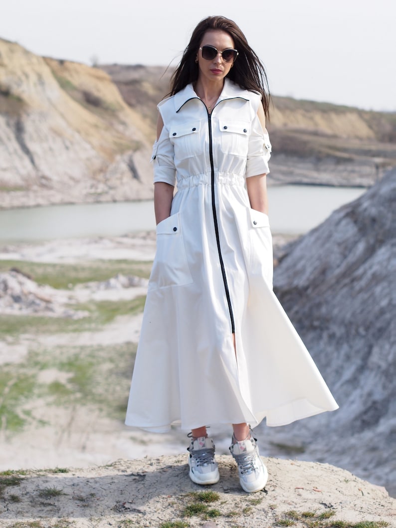 May include: A white long-sleeved dress with a zipper closure, a cinched waist, and cut-out shoulders. The dress has two large pockets on the front and is worn with gray sneakers.