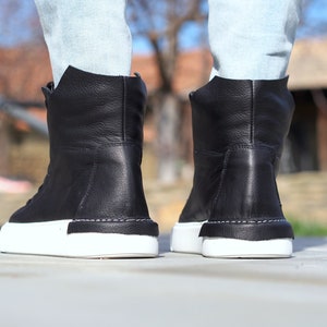 May include: Black leather high-top sneakers with white soles. The shoes have a simple design and are made of high-quality materials.