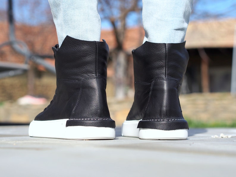 May include: Black leather high-top sneakers with white soles. The shoes have a simple design and are made of high-quality materials.