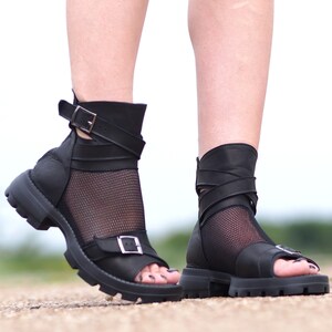 K&ouml;nnte beinhalten: Schwarze Ledersandalen mit einem Mesh-Einsatz und Schnallenverschl&uuml;ssen. Die Sandalen haben eine dicke Plateau-Sohle.