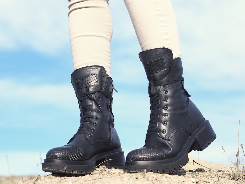 K&ouml;nnte beinhalten: Ein Paar schwarze Lederstiefel mit Schn&uuml;rung und einem dicken Absatz. Die Stiefel haben ein strukturiertes Muster an der Spitze und einen Rei&szlig;verschluss an der Seite.