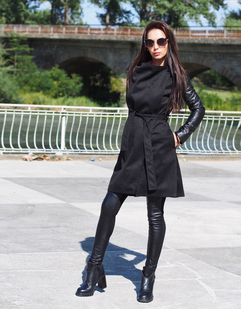 May include: A black long-sleeved coat with leather sleeves and a belt. The coat is worn over black leggings and black ankle boots.