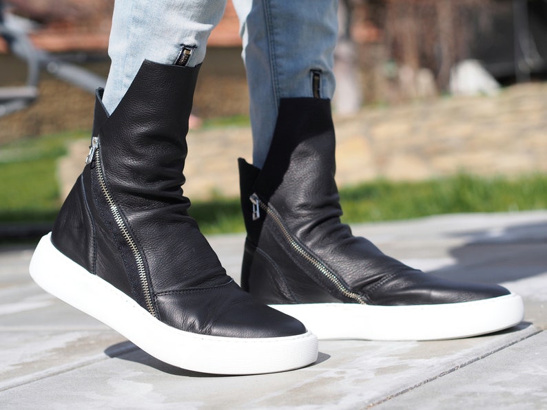 Puede incluir: Botas de tobillo de cuero negro con suela de plataforma blanca y cremallera lateral. Las botas est&aacute;n ligeramente ca&iacute;das y tienen un aspecto informal.