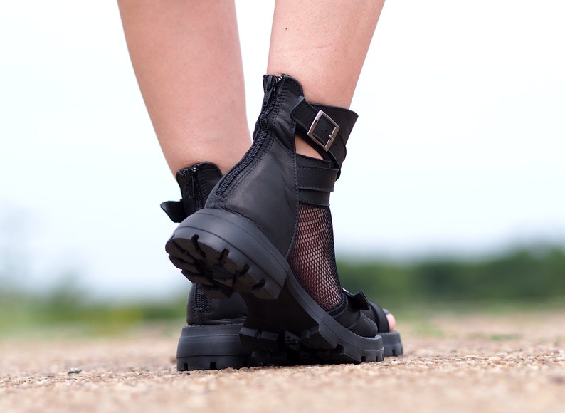 K&ouml;nnte beinhalten: Schwarze Ledersandalen mit Rei&szlig;verschluss an der R&uuml;ckseite und einem Schnallenriemen um den Kn&ouml;chel. Die Sandalen haben eine klobige Plateausohle und eine Netzsocke.
