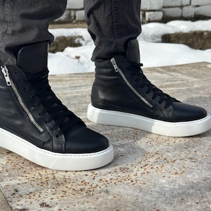 May include: Black leather high-top trainers with white soles and a zip detail on the side.