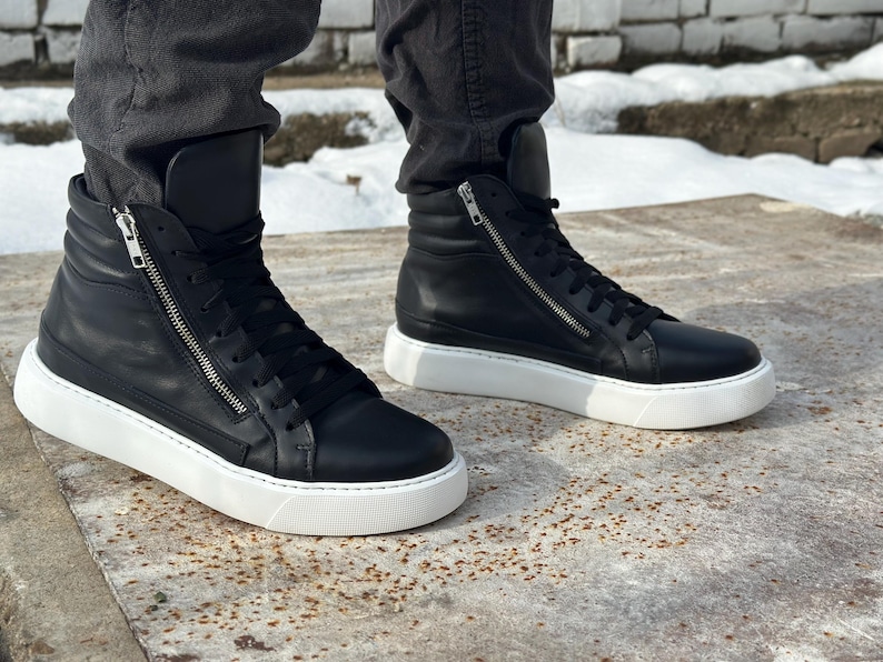 May include: Black leather high-top trainers with white soles and a zip detail on the side.