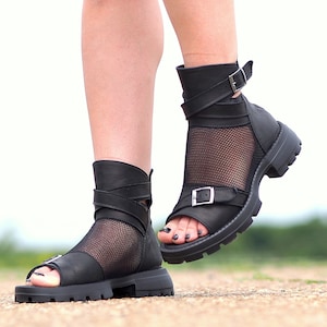K&ouml;nnte beinhalten: Schwarze Ledersandalen mit Mesh-Eins&auml;tzen und Schnallenverschl&uuml;ssen. Die Sandalen haben eine klobige Plateausohle und eine Peeptoe-Form.