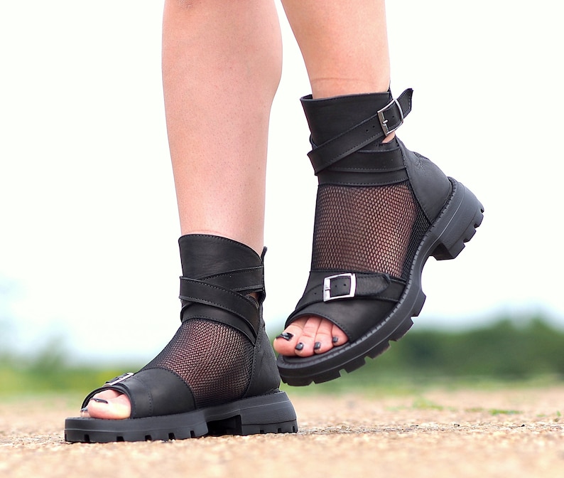 K&ouml;nnte beinhalten: Schwarze Ledersandalen mit Mesh-Eins&auml;tzen und Schnallenverschl&uuml;ssen. Die Sandalen haben eine klobige Plateausohle und eine Peeptoe-Form.