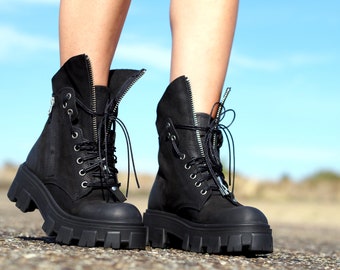 May include: Black leather ankle boots with chunky platform soles and zipper accents. The boots have lace-up closures and are worn on a person's feet.