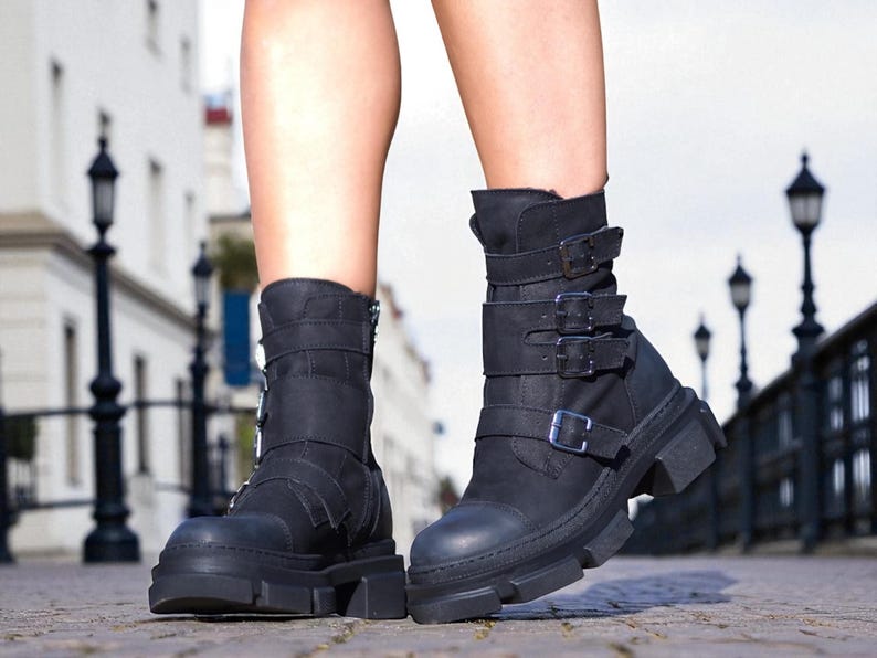 May include: Black ankle boots with multiple straps and buckles. The boots have a chunky sole and a zipper on the side. The boots are made of a matte material and are worn outdoors.