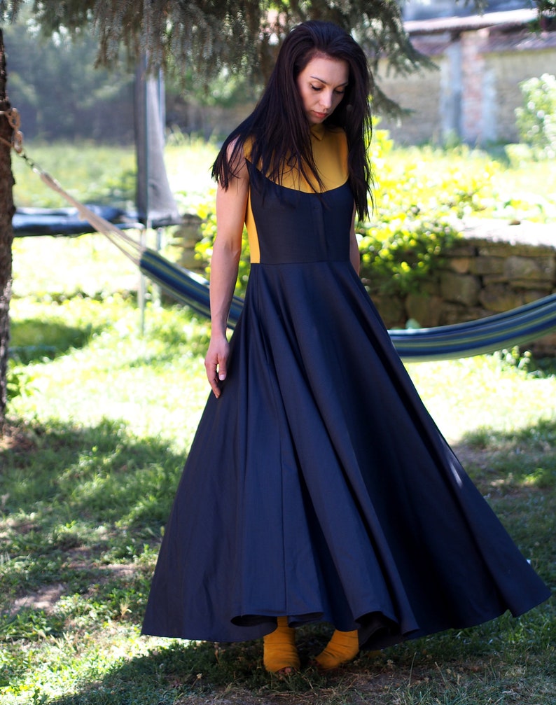 May include: A woman wearing a black and yellow dress with a full skirt. She is standing in a grassy area with a hammock in the background.