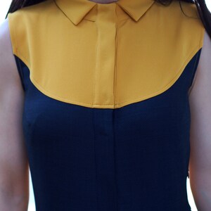 May include: A sleeveless dress with a yellow collar and a navy blue bodice. The dress has a fitted bodice and a flared skirt.