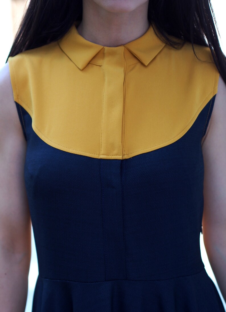 May include: A sleeveless dress with a yellow collar and a navy blue bodice. The dress has a fitted bodice and a flared skirt.