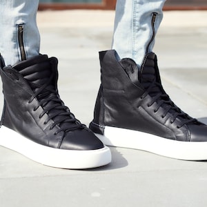 May include: Black high-top sneakers with white soles. The sneakers have a zipper detail on the side and a lace-up closure.