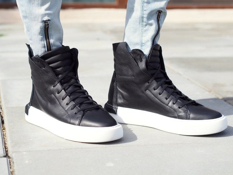 May include: Black high-top sneakers with white soles. The sneakers have a zipper detail on the side and a lace-up closure.