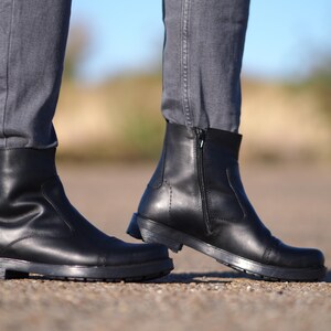 May include: A pair of black leather ankle boots with a side zipper and a rounded toe. The boots have a thick sole and are worn with gray jeans. The boots are approximately 6 inches tall.