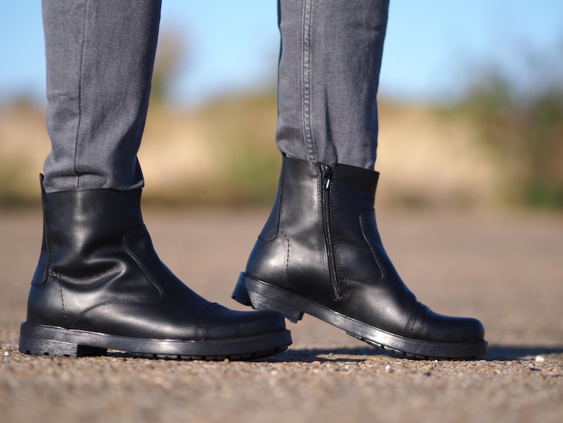 May include: A pair of black leather ankle boots with a side zipper and a rounded toe. The boots have a thick sole and are worn with gray jeans. The boots are approximately 6 inches tall.