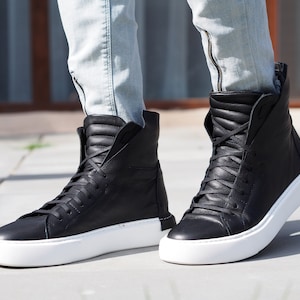 May include: Black leather high-top sneakers with white soles. The sneakers have a zipper on the side and are laced up.