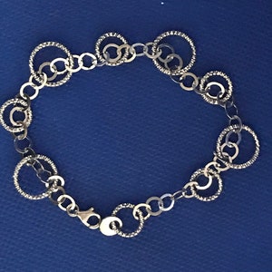 May include: A silver bracelet featuring a chain and multiple interconnected circles. The circles have a textured surface.