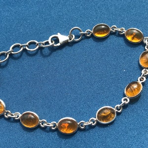 May include: A silver chain bracelet with oval-shaped amber stones. The bracelet has a lobster claw clasp.