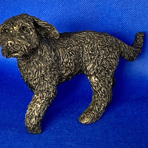 Puede incluir: Una escultura de bronce negro de un perro con pelo rizado. El perro camina con la cabeza girada hacia un lado.