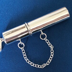 May include: A silver cylindrical pendant with a chain attached. The pendant has a screw-on top and bottom, and the bottom has a small inscription that reads "925".