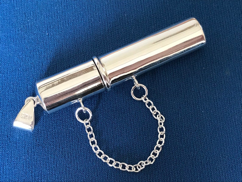 May include: A silver cylindrical pendant with a chain attached. The pendant has a screw-on top and bottom, and the bottom has a small inscription that reads "925".