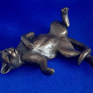 May include: A bronze sculpture of a cat lying on its back with its paws in the air. The cat is made of a dark brown metal and has a realistic appearance.