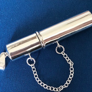 May include: A silver, cylindrical, two-piece pill box with a chain attached. The box is engraved with the number "925" on the bottom.