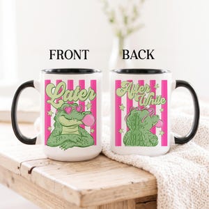 May include: Two white ceramic mugs with black handles and rims. The front mug features a green alligator wearing pink heart-shaped sunglasses and blowing a pink bubble, with the text "Later" above. The back mug shows the alligator from behind with the text "After While". Both have pink vertical stripes and stars.