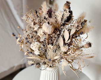 Può includere: Un vaso di ceramica bianca con una texture a coste contiene un bouquet di fiori secchi in tonalità beige, marrone e bianco. I fiori includono erbe secche, baccelli di semi e piccoli fiori bianchi.