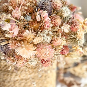 Può includere: Un bouquet di fiori secchi in tonalità rosa, bianco e beige, disposti in un cesto intrecciato. I fiori includono rose secche, respiro di bambino e altri fiori delicati.