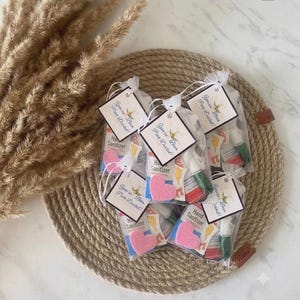 May include: Several small, clear organza drawstring bags containing hand sanitizer bottles, each adorned with a square white tag featuring a bee illustration and the text "You're Been Pure-Duced!" along with a small pink felt heart attached.
