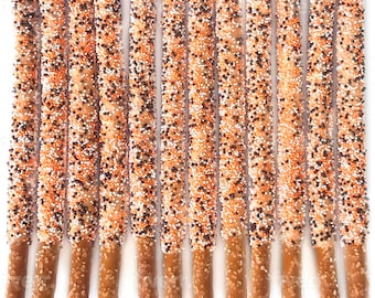 May include: A dozen chocolate-covered pretzel rods, each dipped in white chocolate and sprinkled with orange, brown, and white sprinkles.