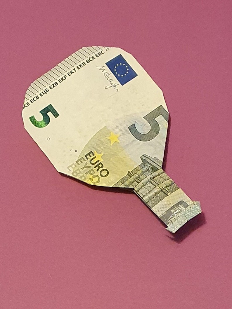 Op de afbeelding: Een briefje van vijf euro gevouwen in de vorm van een peddel. Het briefje is lichtbeige van kleur met een blauw en geel sterrenontwerp. De tekst "ECB ЕЦБ EZB EKP EKT EKB BCE EBC 20" staat bovenaan het briefje gedrukt. De tekst "5" staat in het midden van het briefje gedrukt. De tekst "EURO" staat onderaan het briefje gedrukt.