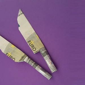 Może przedstawiać: Dwa noże origami wykonane z banknotów euro na fioletowym tle. Noże są złożone tak, aby przypominały tradycyjny nóż z ostrzem i rękojeścią.