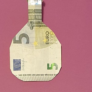Op de afbeelding: Een 5 eurobiljet gevouwen in de vorm van een fles. Het biljet is groen en wit met een ster en het woord "EURO" erop gedrukt.