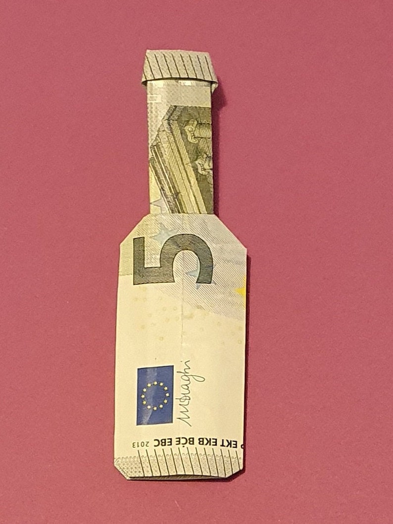 Op de afbeelding: Een briefje van vijf euro gevouwen in de vorm van een fles. Het briefje is lichtgroen van kleur met een afbeelding van een gebouw erop. Op het briefje staat "EKT EKB BCE EBC 2013" en "euro" gedrukt.