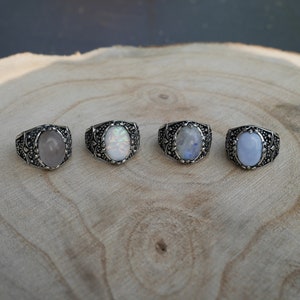 Peut inclure: Quatre bagues en argent avec des pierres précieuses de forme ovale. Les bagues ont des motifs complexes et présentent une pierre précieuse rose, blanche, blanche irisée et bleue.