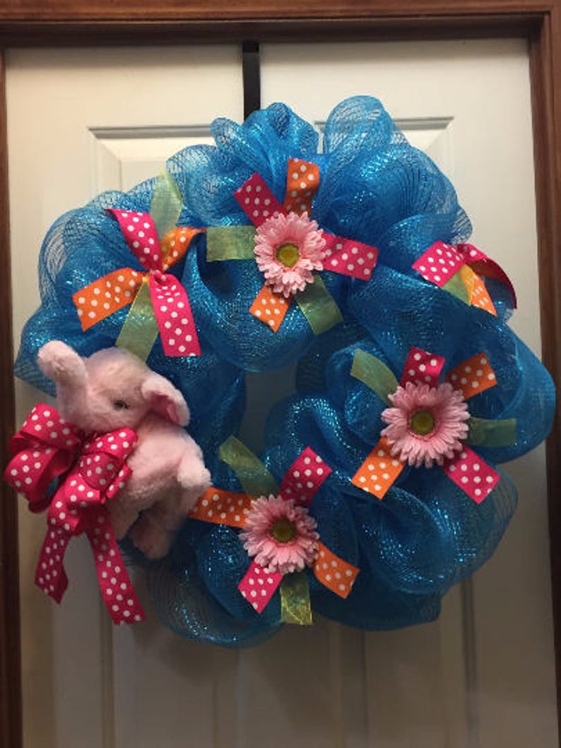 May include: A blue mesh wreath decorated with pink and orange polka dot bows, pink flowers, and a pink plush elephant.