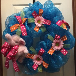 May include: A blue mesh wreath decorated with pink and orange polka dot ribbon, pink flowers, and a pink elephant plush toy.