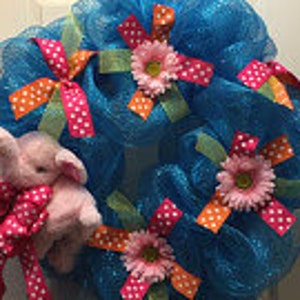 May include: A turquoise mesh wreath decorated with pink and orange polka dot ribbon, pink flowers, and a pink plush elephant.