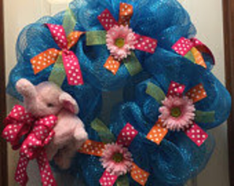 May include: A turquoise mesh wreath decorated with pink and orange polka dot ribbon, pink flowers, and a pink plush elephant.
