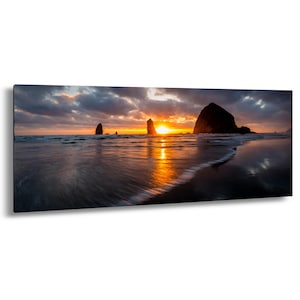 Könnte beinhalten: Panorama-Leinwanddruck eines Sonnenuntergangs über einem Strand. Der Himmel ist mit dunklen, dramatischen Wolken gefüllt, wobei die Sonne in einem Ausbruch von Orange und Gelb durchbricht. Das Meer spiegelt die Farben des Himmels wider, und mehrere Felsformationen sind sichtbar.