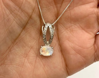 Può includere: Una collana a catena d'argento con un ciondolo in pietra di luna. Il ciondolo è incastonato in una cornice d'argento con piccoli pietre chiare intorno al bordo.