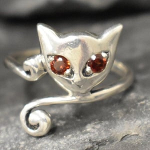 May include: A silver ring with a cat design. The cat has red gemstone eyes.
